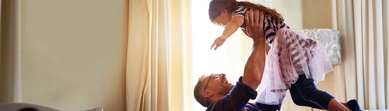 dad holding up young daughter, both laughing